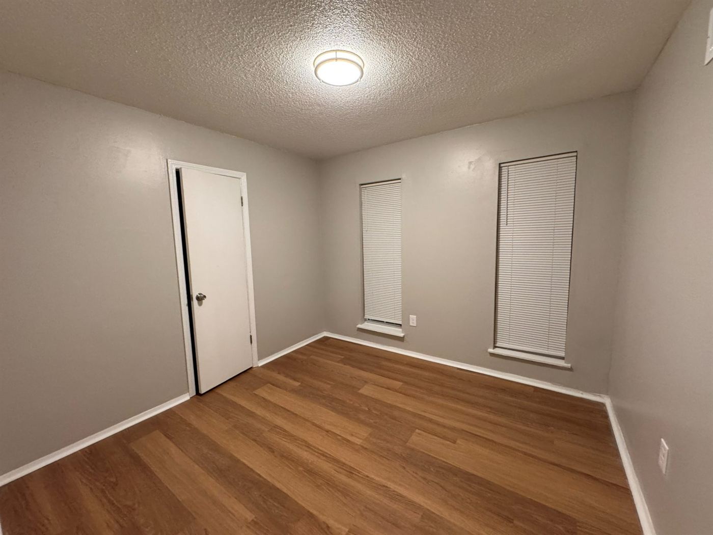 Restored bedroom with new plank flooring, fresh neutral paint, restored windows with new blinds, and new flush-mount lighting by Delta Construction in Memphis, TN