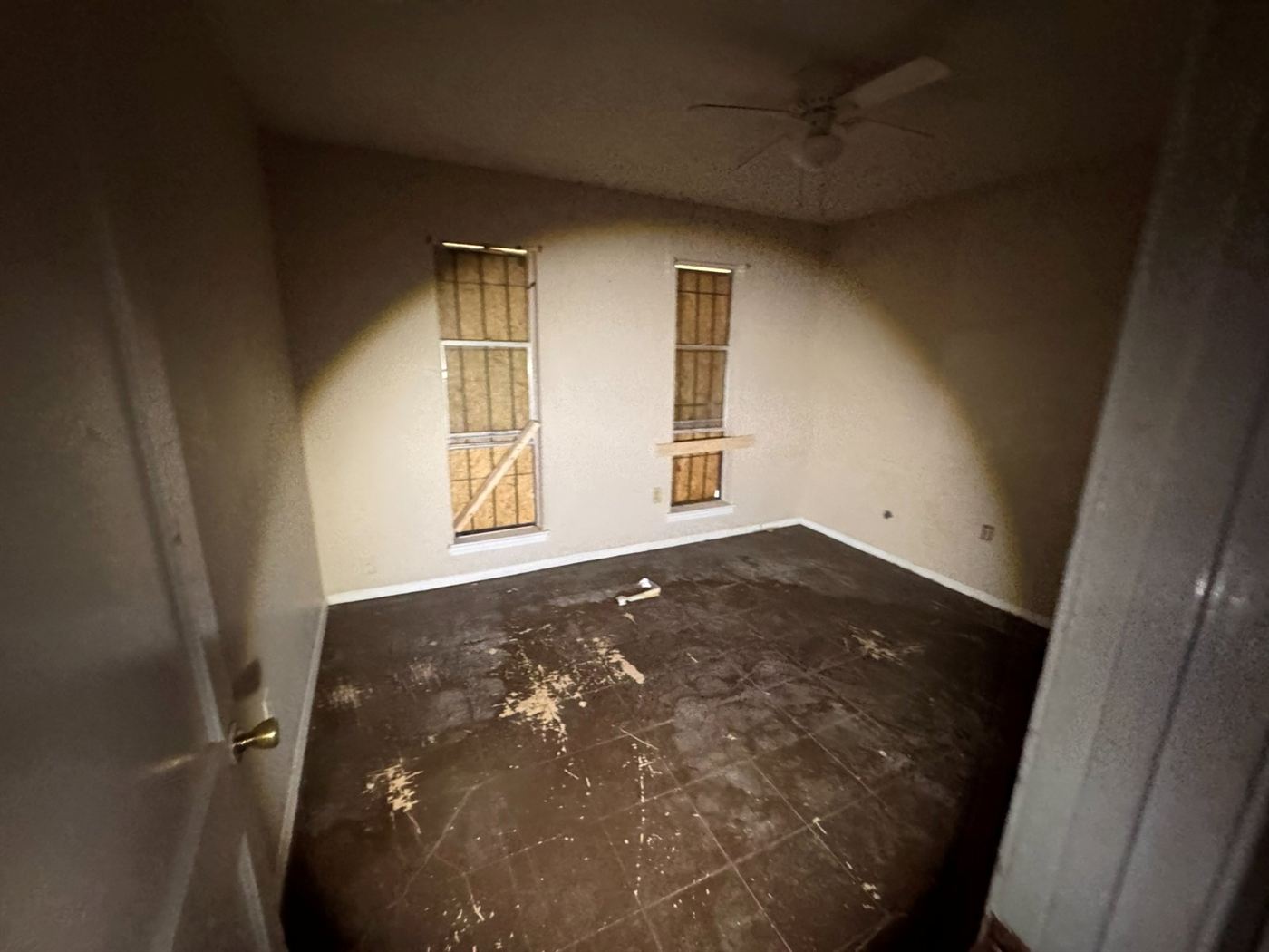 Dark bedroom with boarded-over windows and ruined flooring before restoration in Memphis, TN