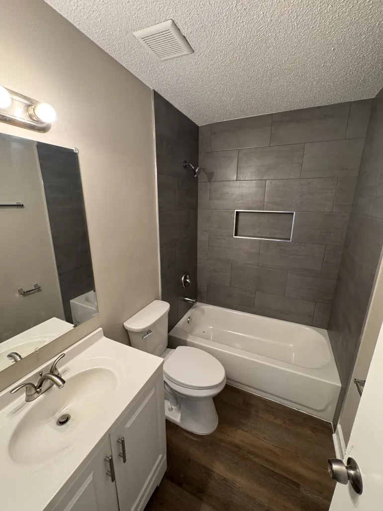 Renovated bathroom with new tile tub surround, vanity, and plank flooring by Delta Construction in Memphis, TN